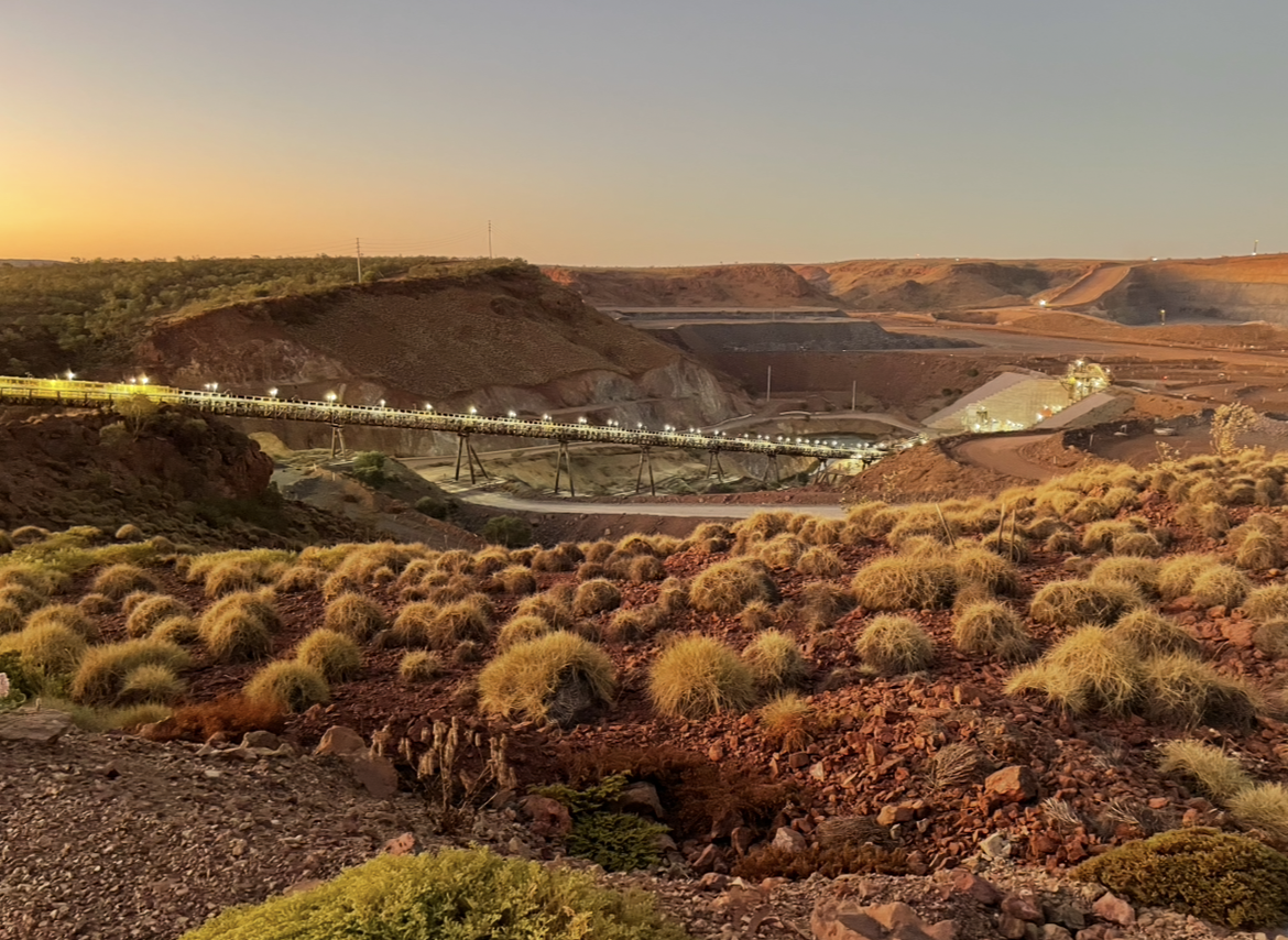 Open-pit mine and illuminated conveyor at sunset